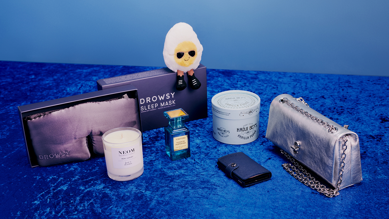 A woman in a checkered dress poses with a giant apple sculpture, holding a small black purse.