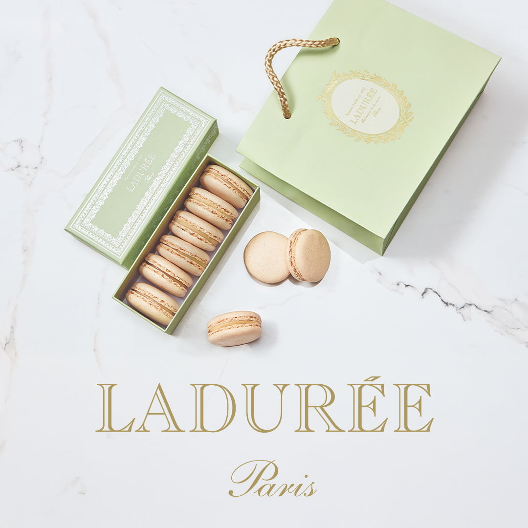 Box of macarons next to a green Ladurée bag on a marble surface.