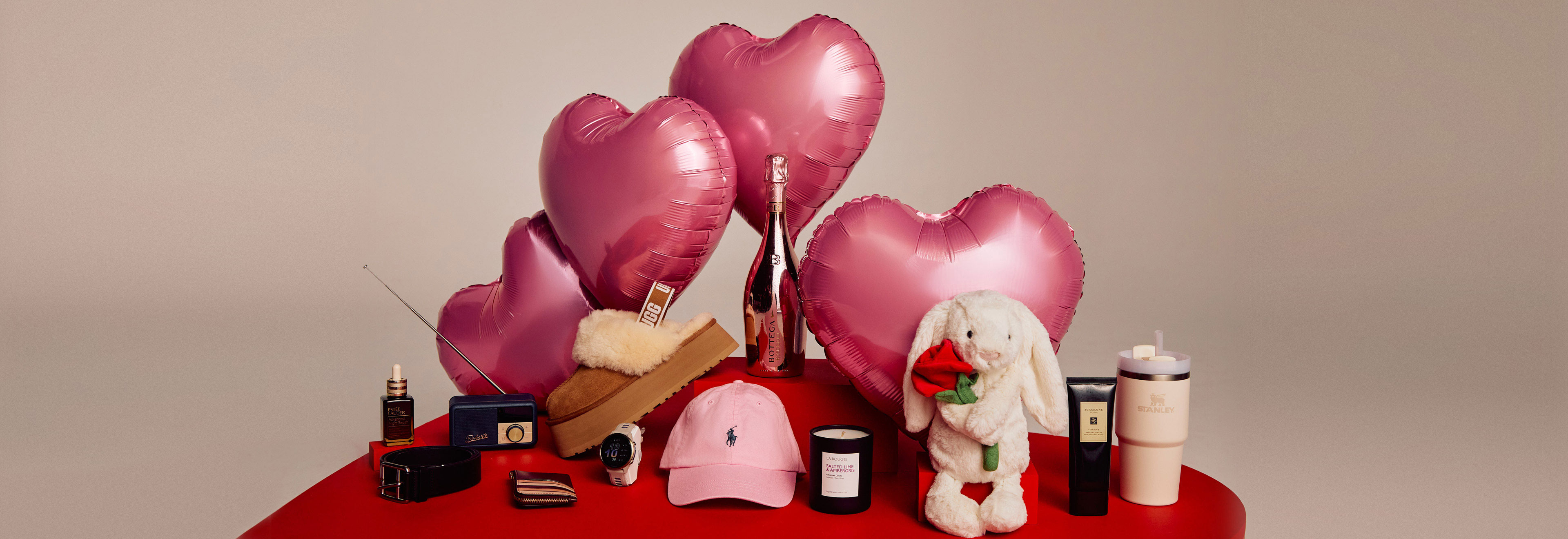 A red table with pink heart-shaped balloons, a stuffed bunny, candles, a pink cap, and various small items.