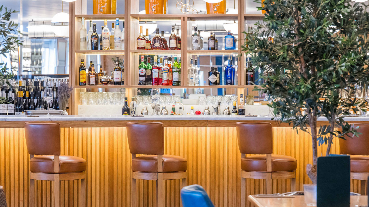 Bar at Browns Brasserie Dublin with leather stools, illuminated shelves, and various bottles.