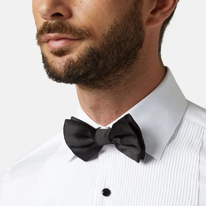 Man wearing a white tuxedo shirt with black buttons and a black bow tie.
