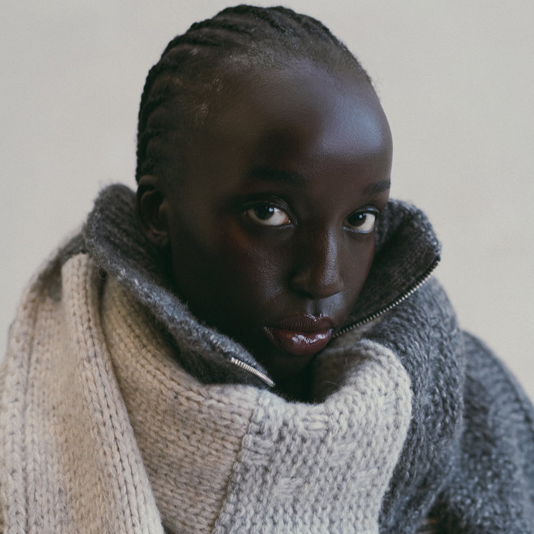 Person wearing a heavy knit sweater and a jacket, looking directly at the camera with an intense gaze.