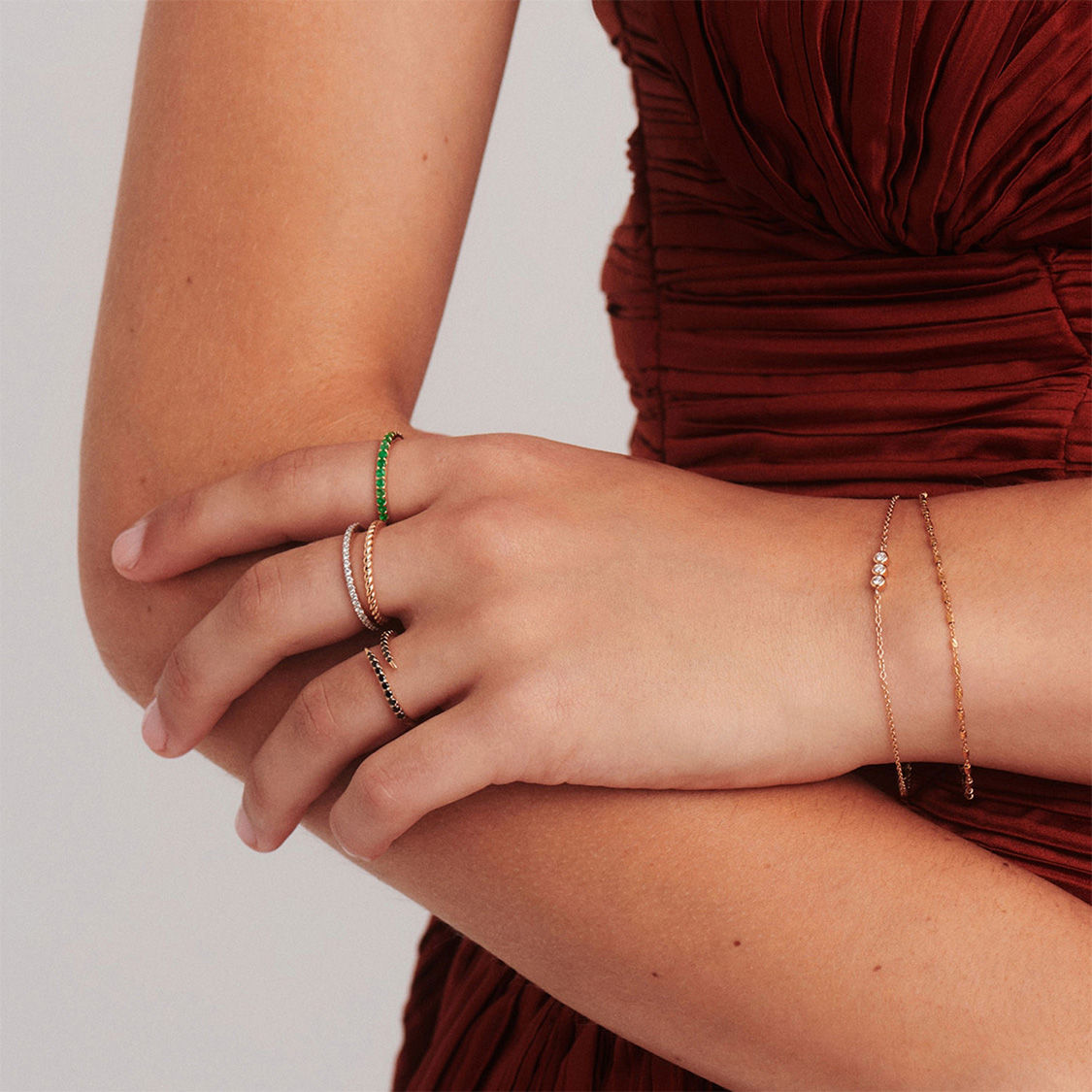 Person wearing a red dress with layered rings and a delicate bracelet, hands gently crossed.
