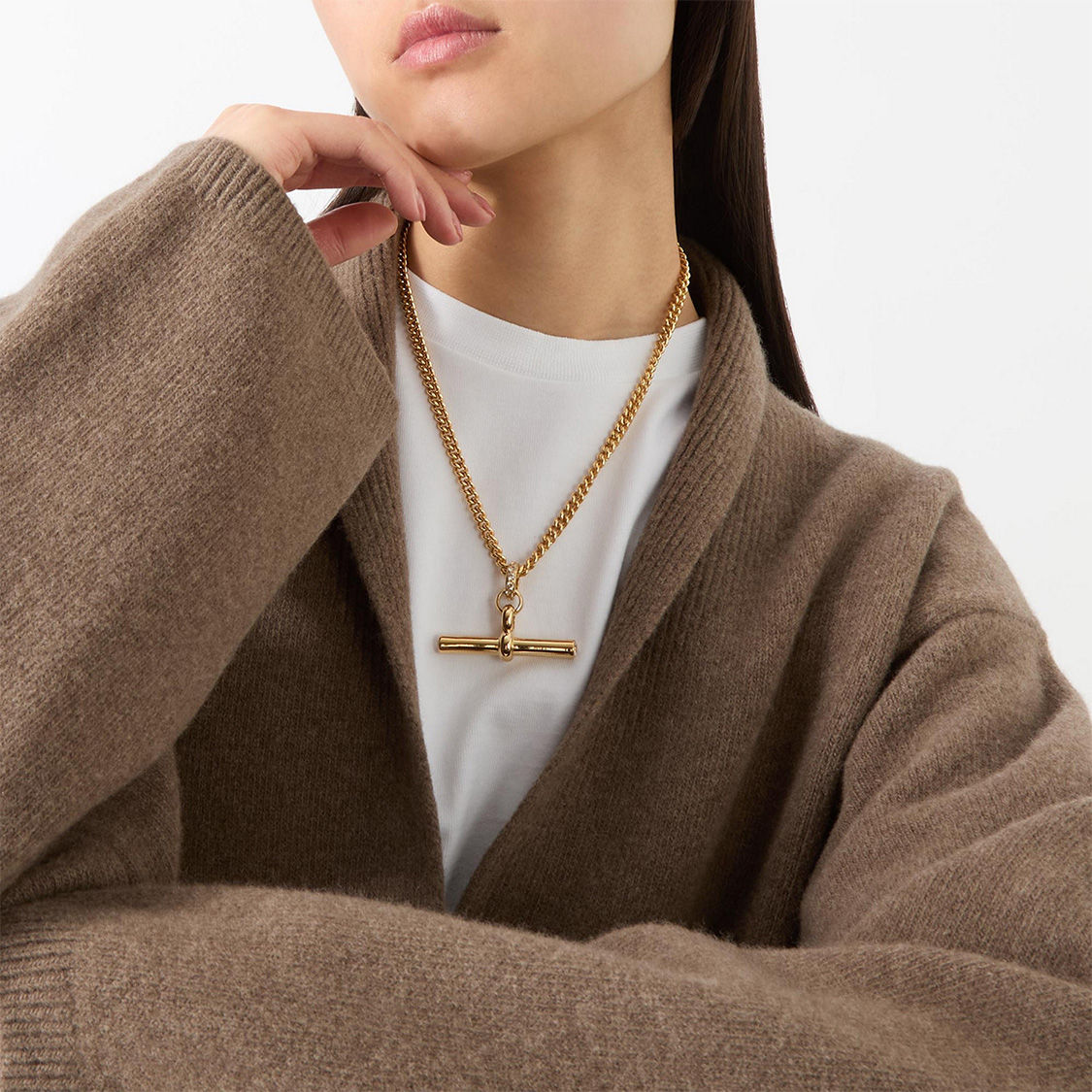 Person wearing a brown cardigan and a gold chain necklace with a bar pendant.