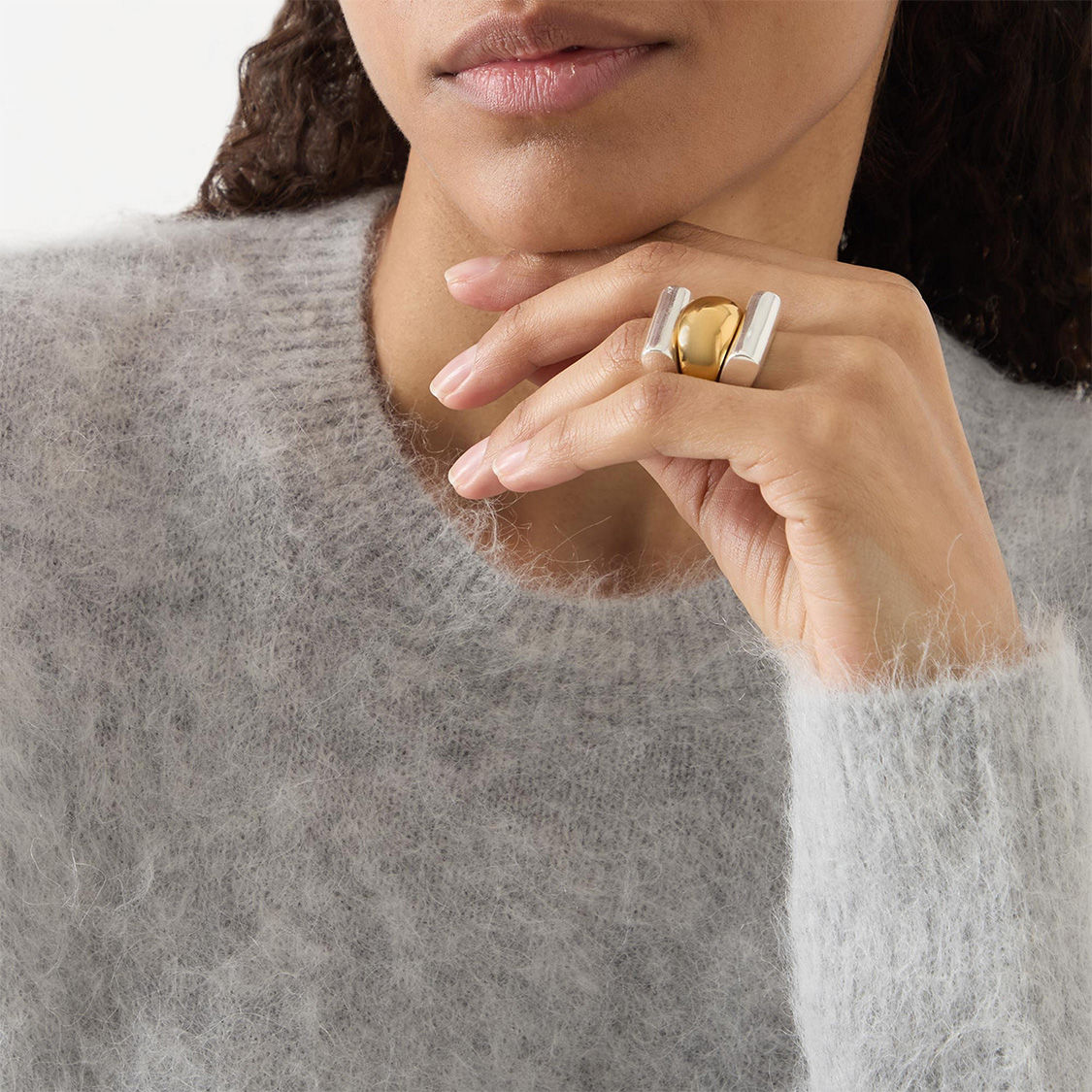 A person wearing a fuzzy sweater displays a large, stylish ring on their finger.