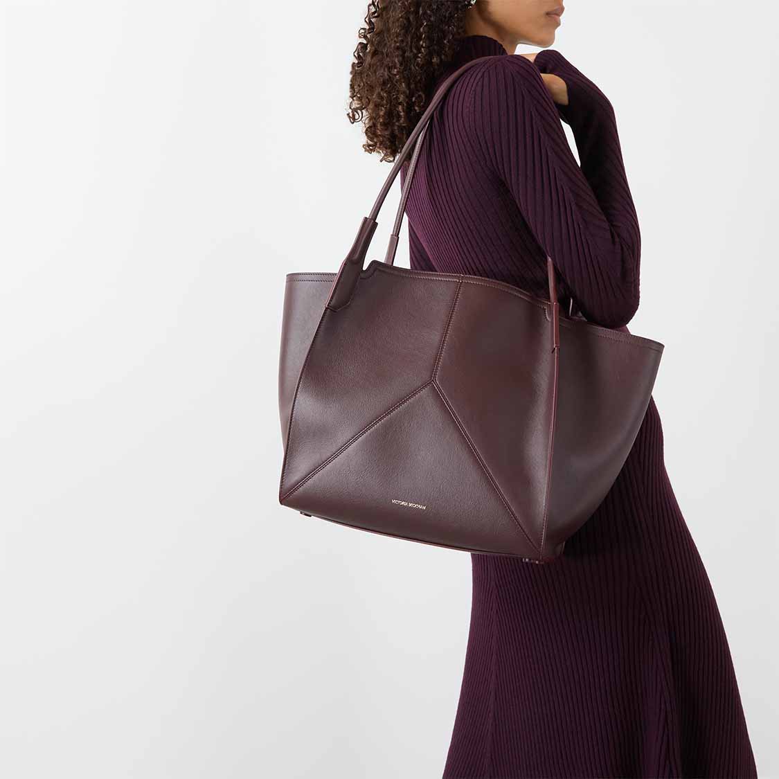 Woman in a purple knit dress carries a large brown leather tote.