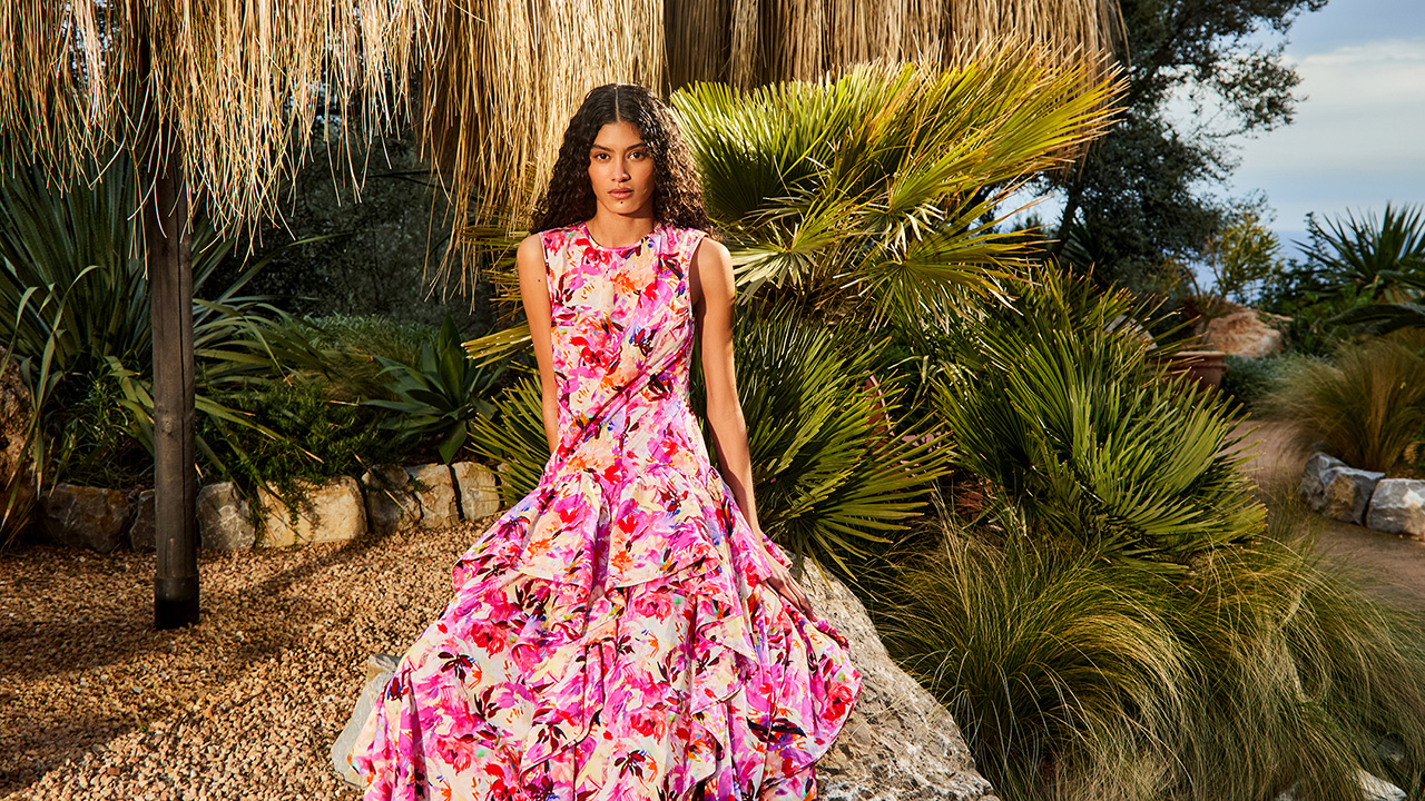 A person in a vibrant floral dress sitting on a rock, surrounded by lush tropical plants.