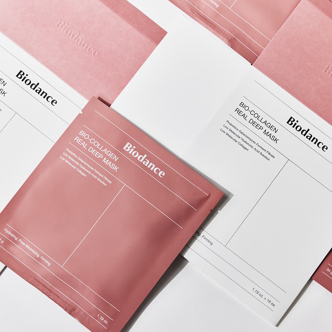Several packets of Biodance Bio-Collagen Real Deep Mask are arranged in a grid pattern. The packets are in shades of pink and white, with minimalist design and text. The layout is neat and aesthetically pleasing, highlighting the skincare product's packaging.