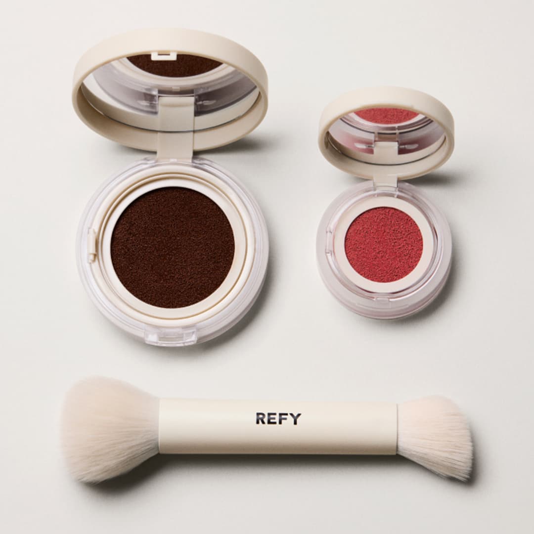 Makeup set featuring a large brown compact, a smaller pink compact, and a dual-ended white makeup brush with 'REFY' printed on it. The items are arranged neatly on a light background.