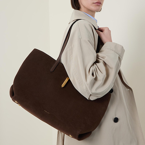 Person in a beige trench coat holding a large brown tote bag.