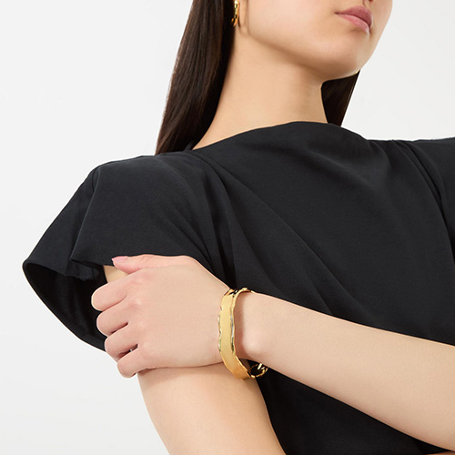 A woman wearing a black top and gold bracelet with her arms crossed.
