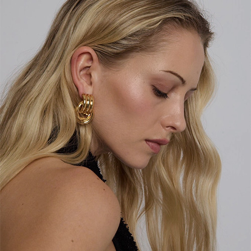 A woman with long blonde hair wears large gold earrings, looking downwards.