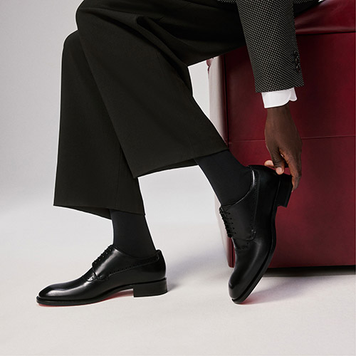 Person wearing black dress shoes, dark trousers, and a suit jacket, sitting on a red bench.