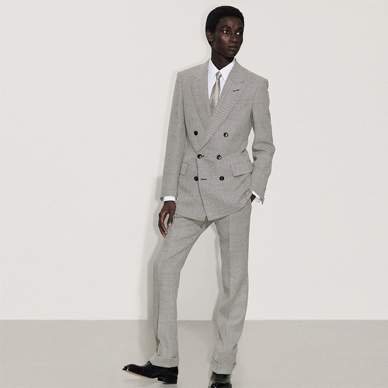 A person in a double-breasted grey suit with a white shirt and tie, standing against a plain background.