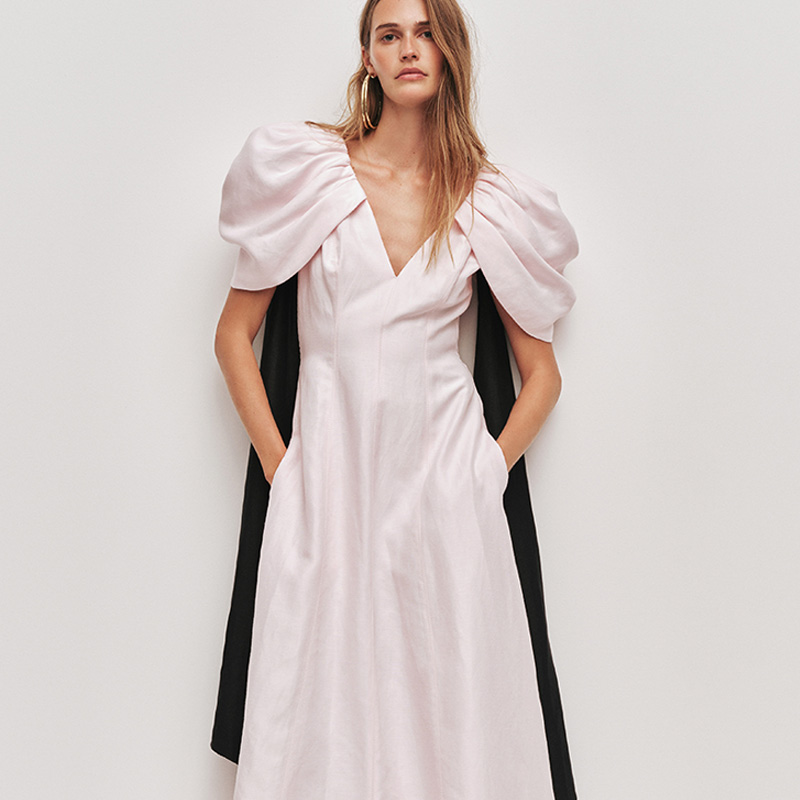 Woman in a white dress with large puff sleeves, hands in pockets, and wearing hoop earrings.