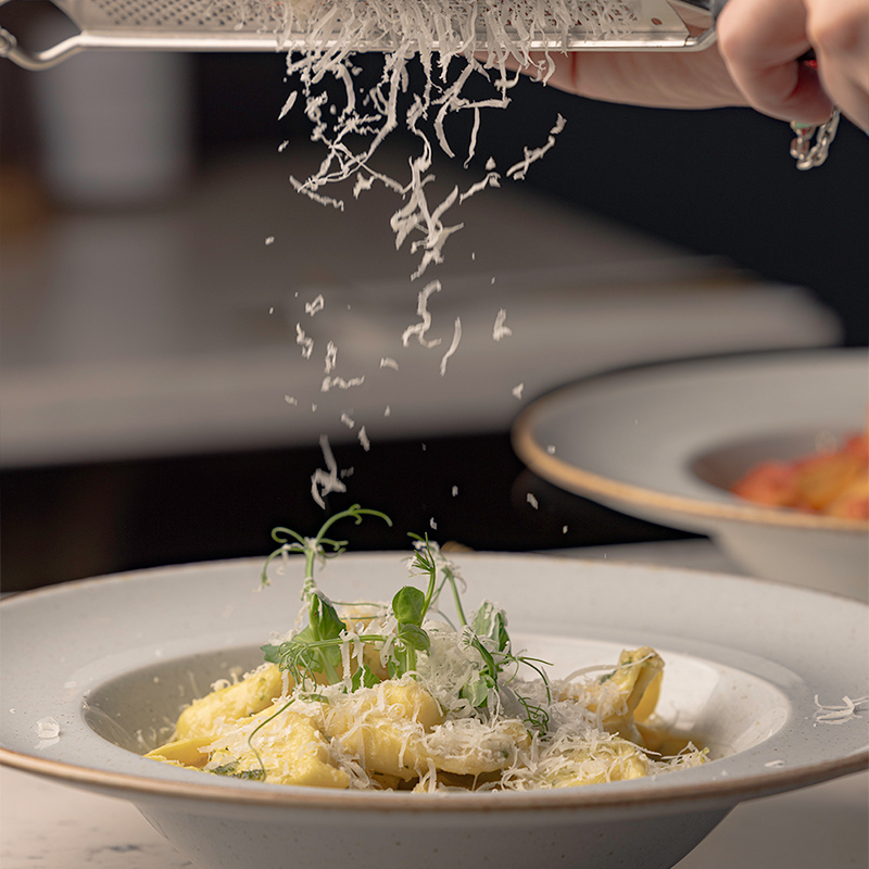 A dish of pasta garnished with fresh greens and sprinkled with cheese in a white bowl.