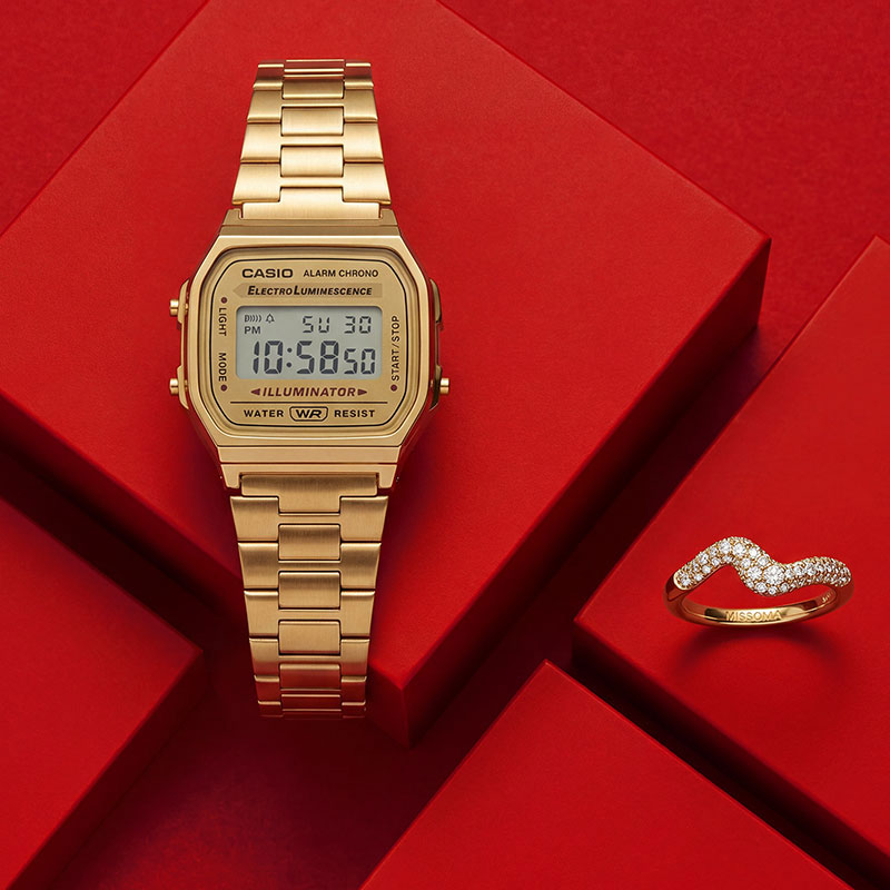 Gold Casio digital watch and a sparkling ring displayed on a red background.

