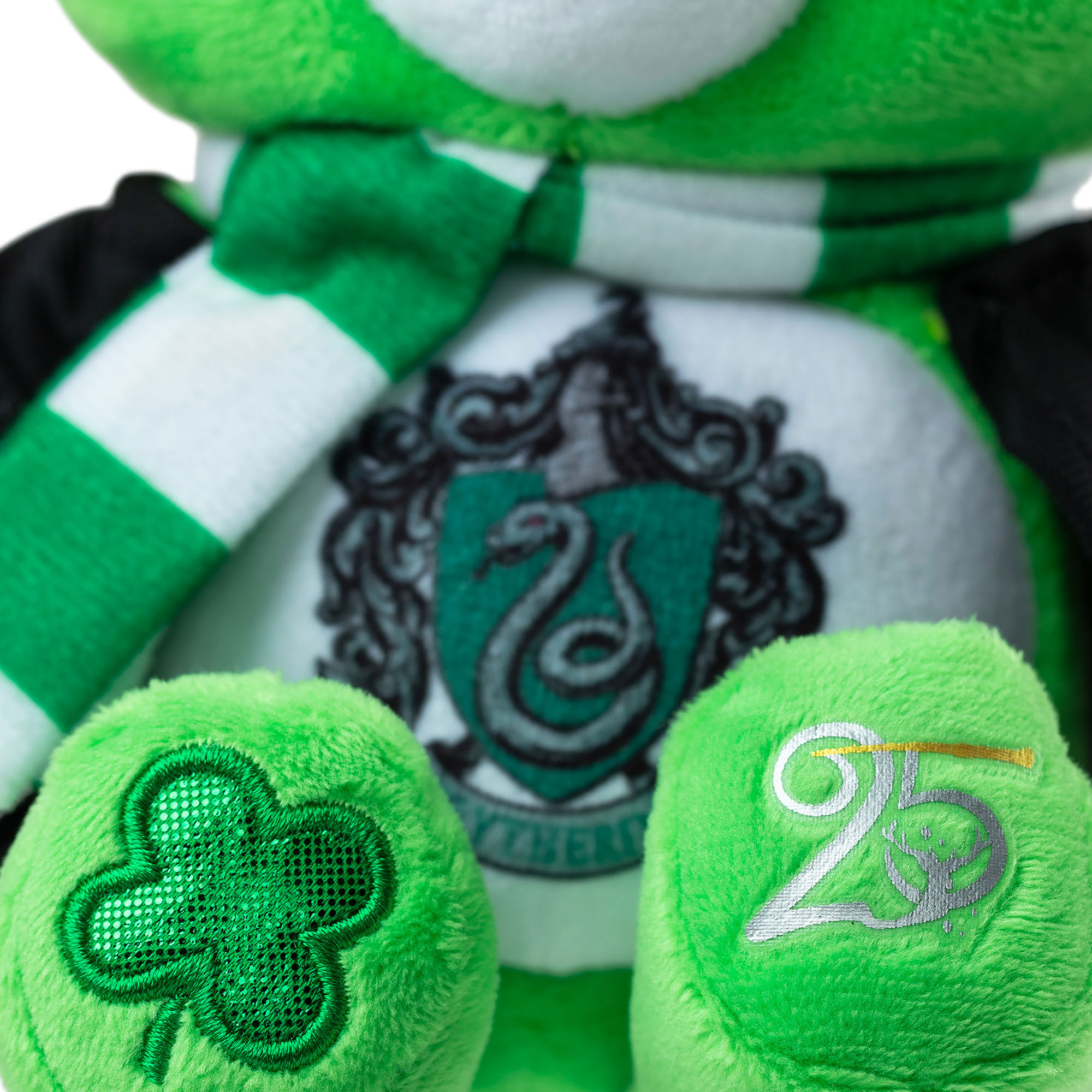 Care Bears green Slytherin plush bear close-up showing embroidered crest, striped scarf, shamrock and 25th anniversary detail on paws