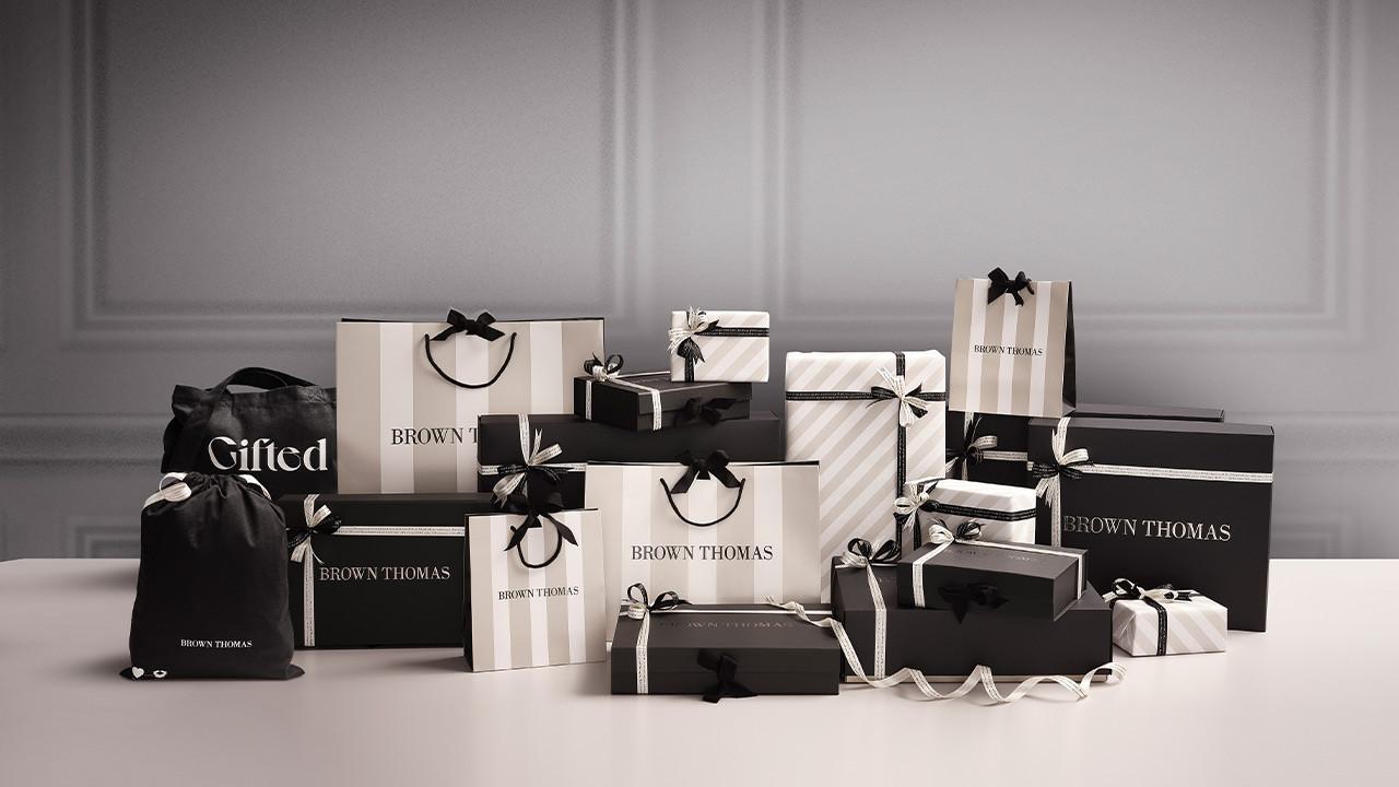 A display of Brown Thomas gift bags and boxes in black, white, and striped patterns with ribbons.