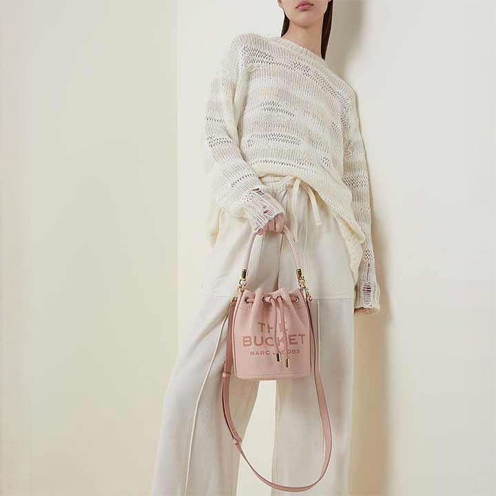 On the left, various pink handbags are displayed. On the right, a person in a light outfit holds a pink bucket bag.
