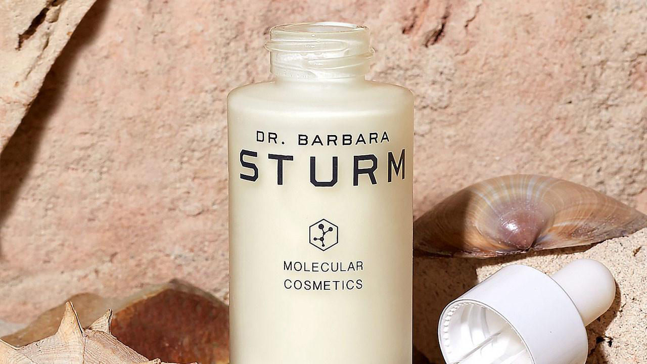 Travel size beauty product by Dr. Barbara Sturm, set against a textured background with natural elements.

