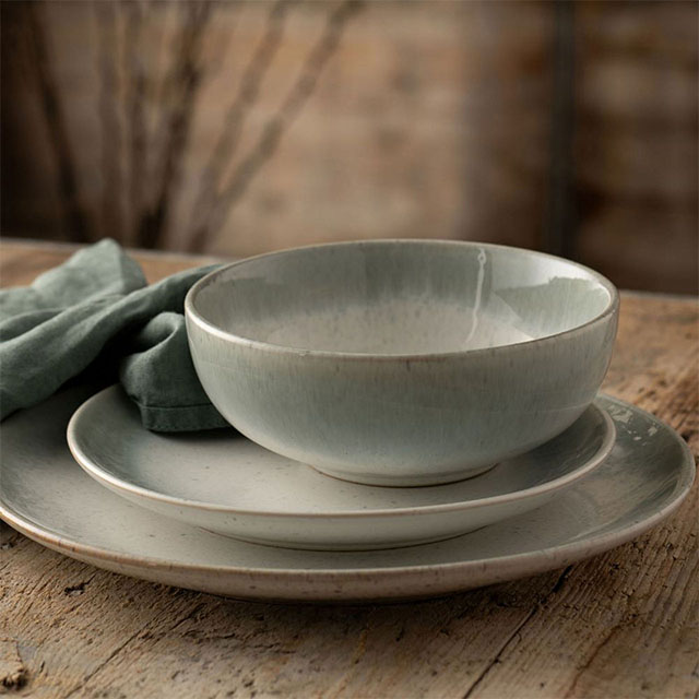 Stacked rustic ceramic bowl and plates with a green cloth on a wooden table.