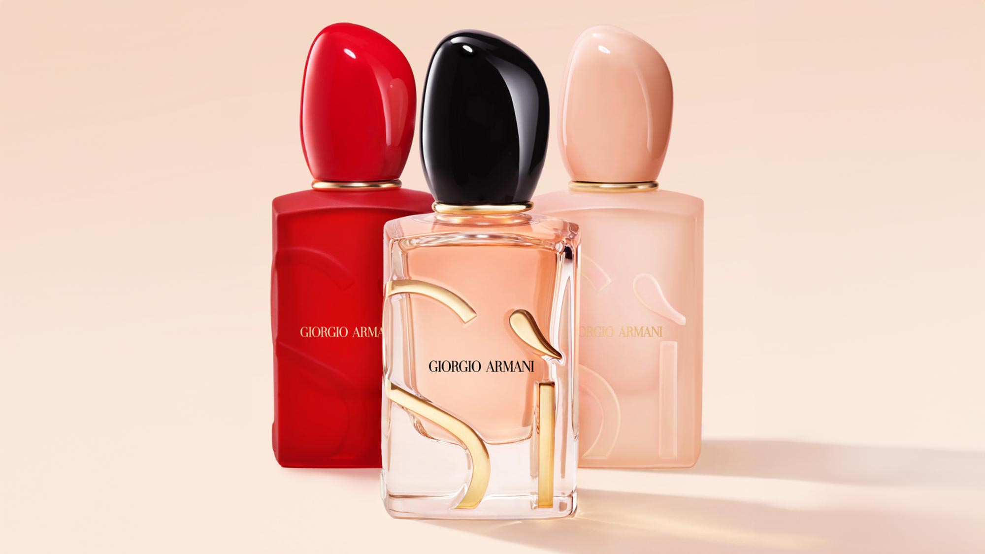 Three Giorgio Armani Sì fragrance bottles in red, black and nude shades with gold accents on neutral background