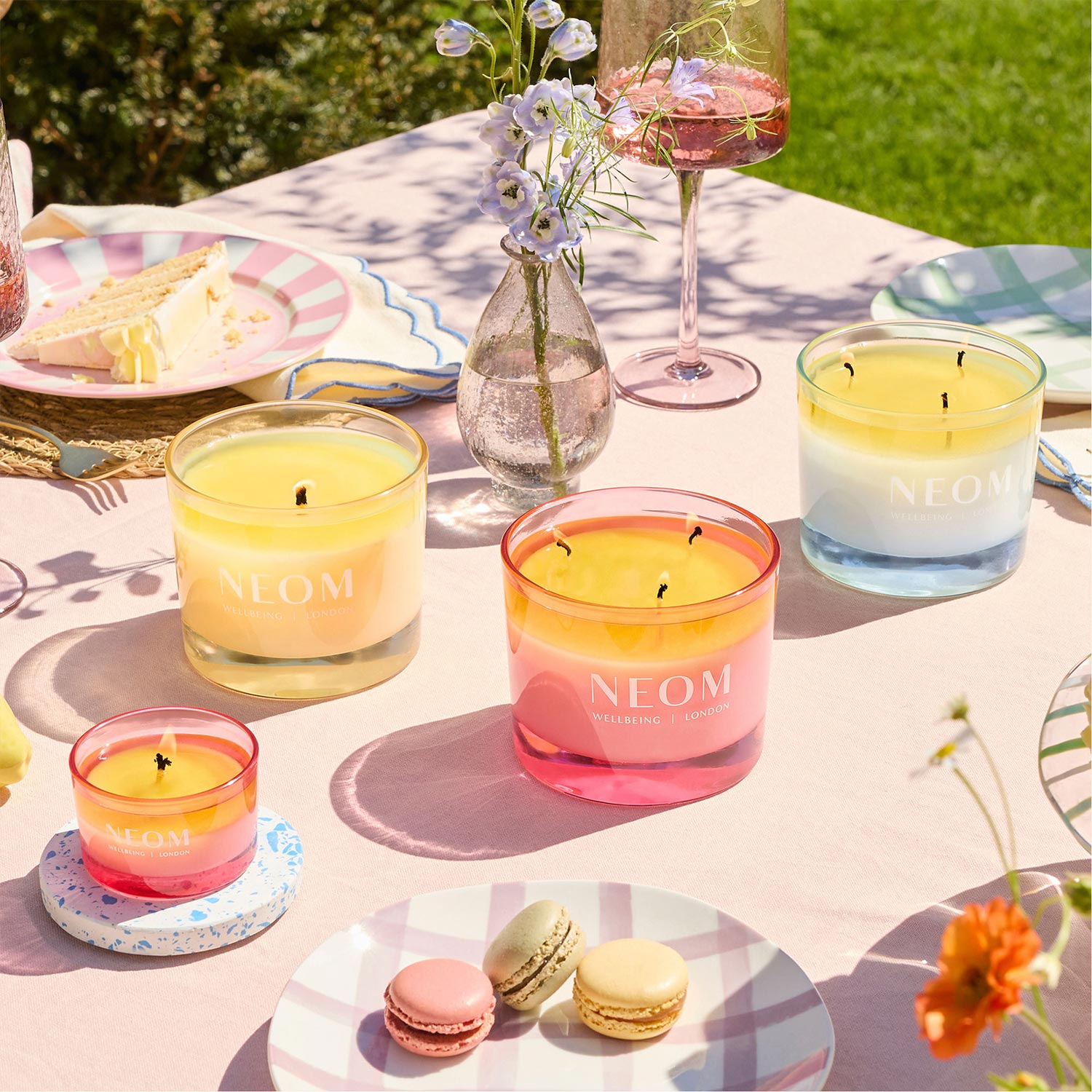 A colorful outdoor table setup with candles, macarons, a vase of flowers, and drinks on a sunny day.