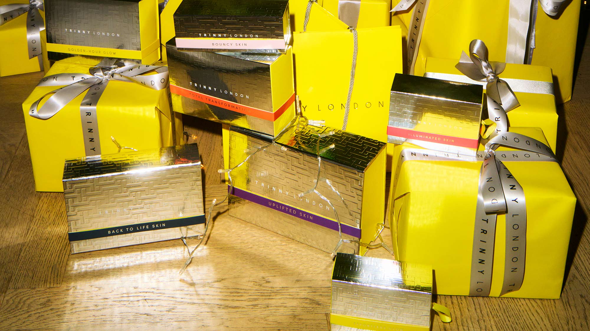 Stacks of yellow and gold gift boxes with silver ribbons on a wooden floor.