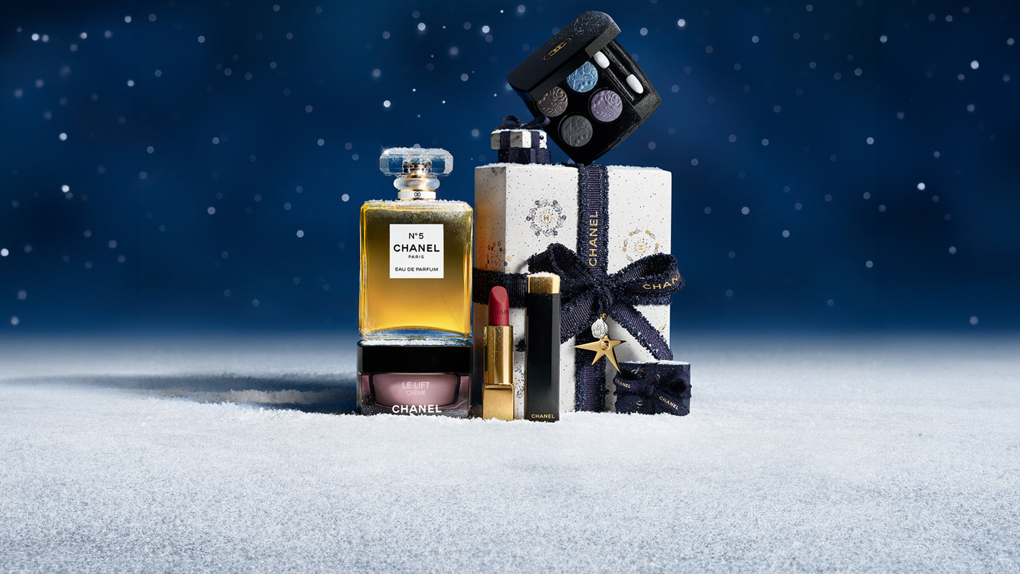 Chanel products, including perfume, lipstick, and eyeshadow, are displayed on snow with a starry night background.