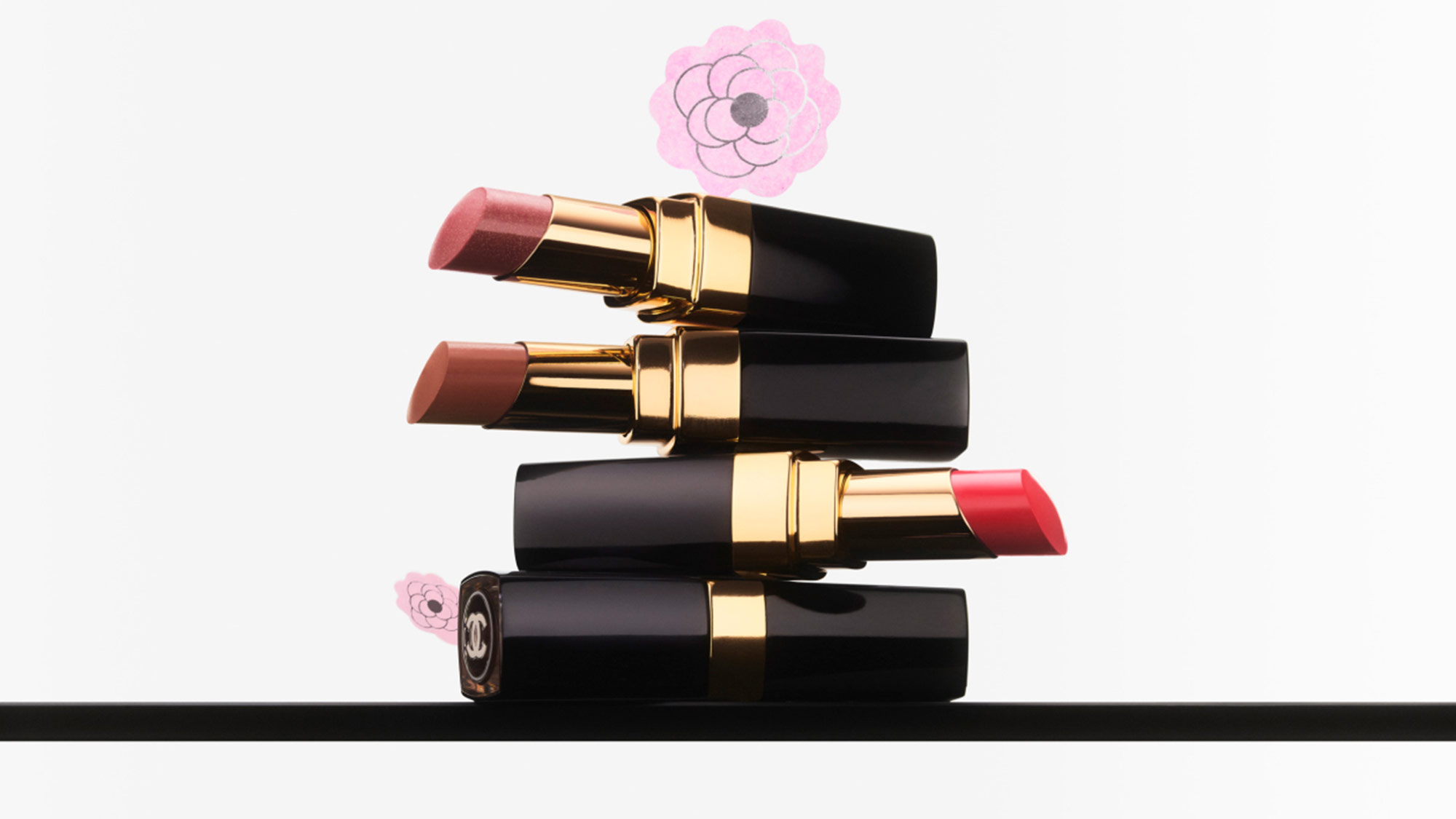 Three lipsticks stacked horizontally with gold accents, set against a white background with pink floral designs.