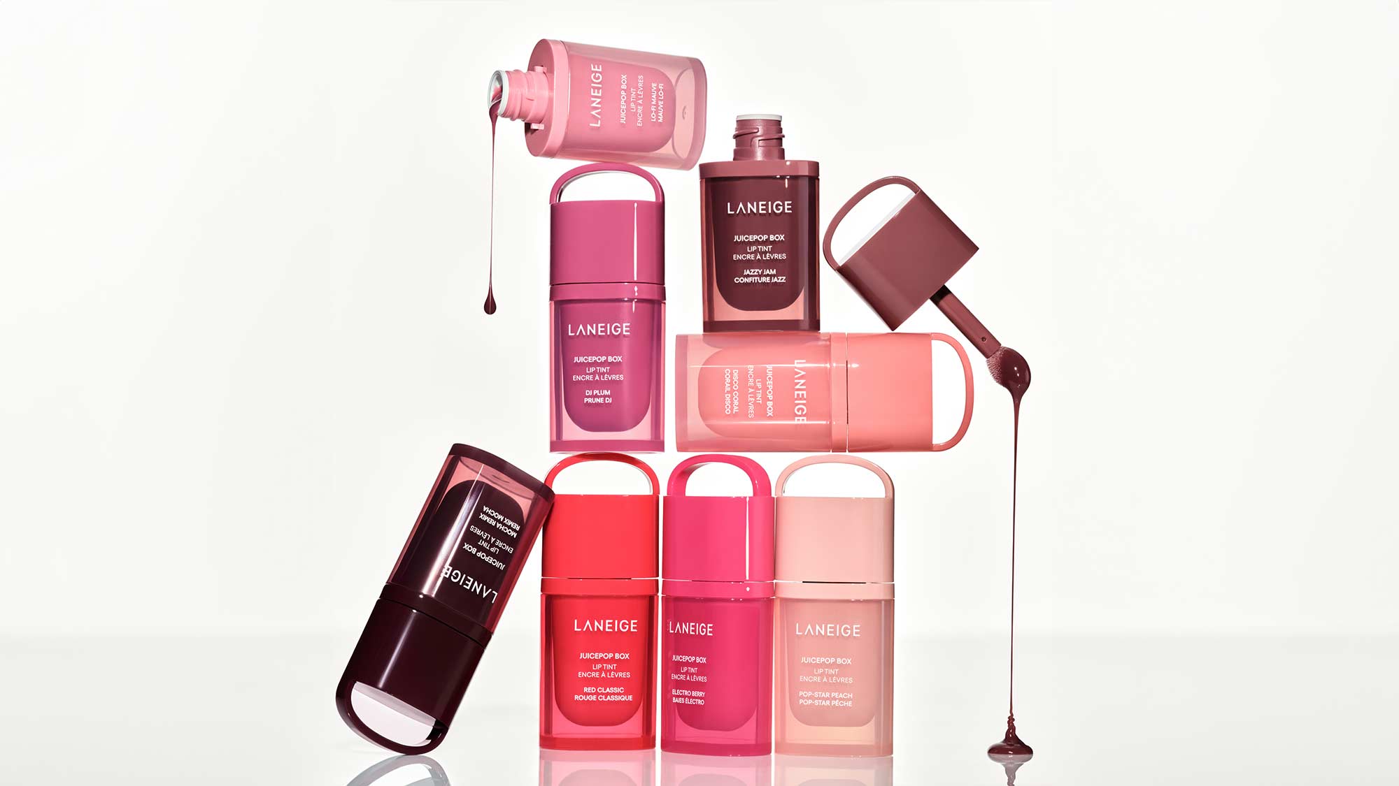 Assorted Laneige makeup products, including liquid and stick formats, in various shades of pink and red, stacked and arranged artistically.