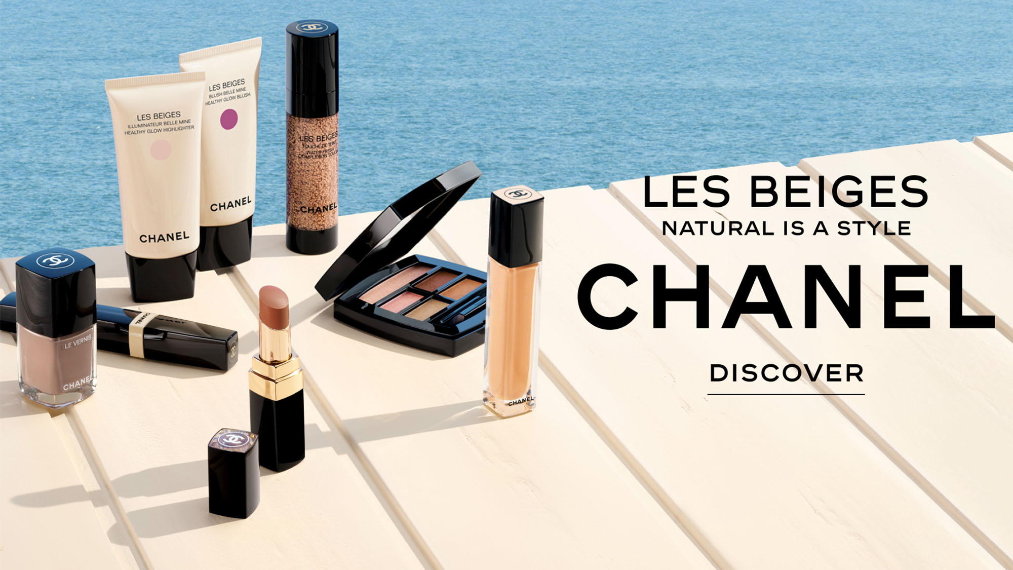 Chanel makeup products displayed on a wooden surface by the water, with 'Les Beiges, Natural is a Style' text.