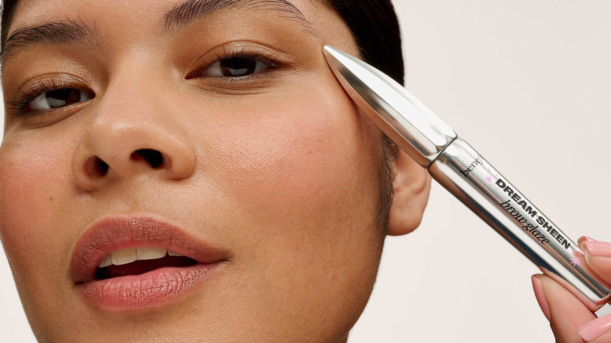 Woman applying Benefit Dream Sheen brow glaze product to eyebrow with applicator brush.