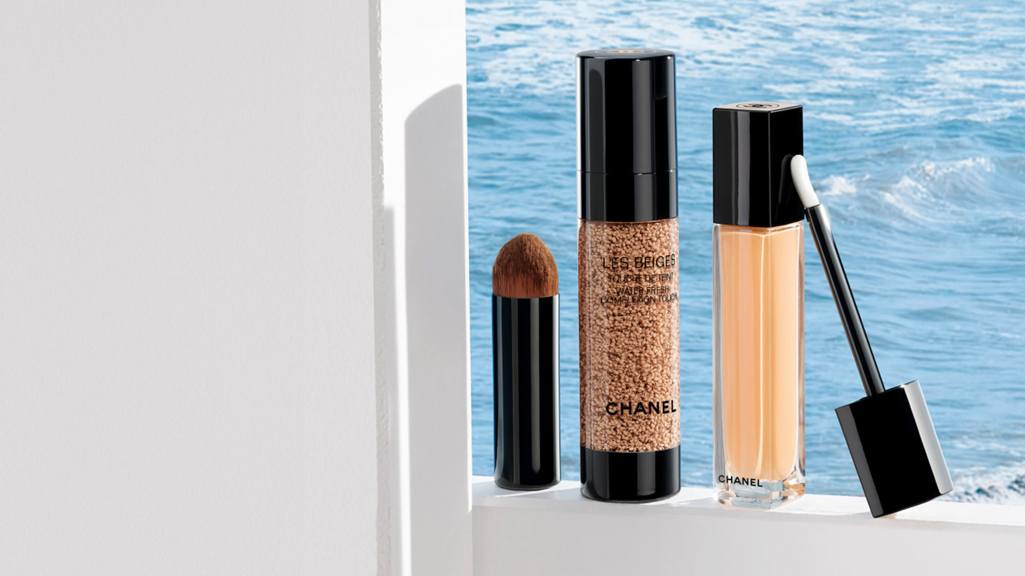 Chanel Les Beiges makeup collection with brush, textured foundation, and liquid cosmetic displayed by seaside