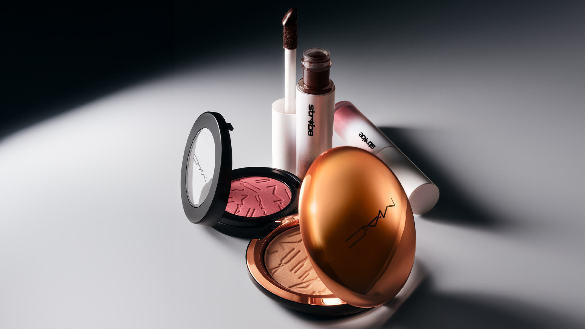 M.A.C. summer makeup products including bronze shimmer powder compact, pink cream blush, and liquid highlighter on white surface.