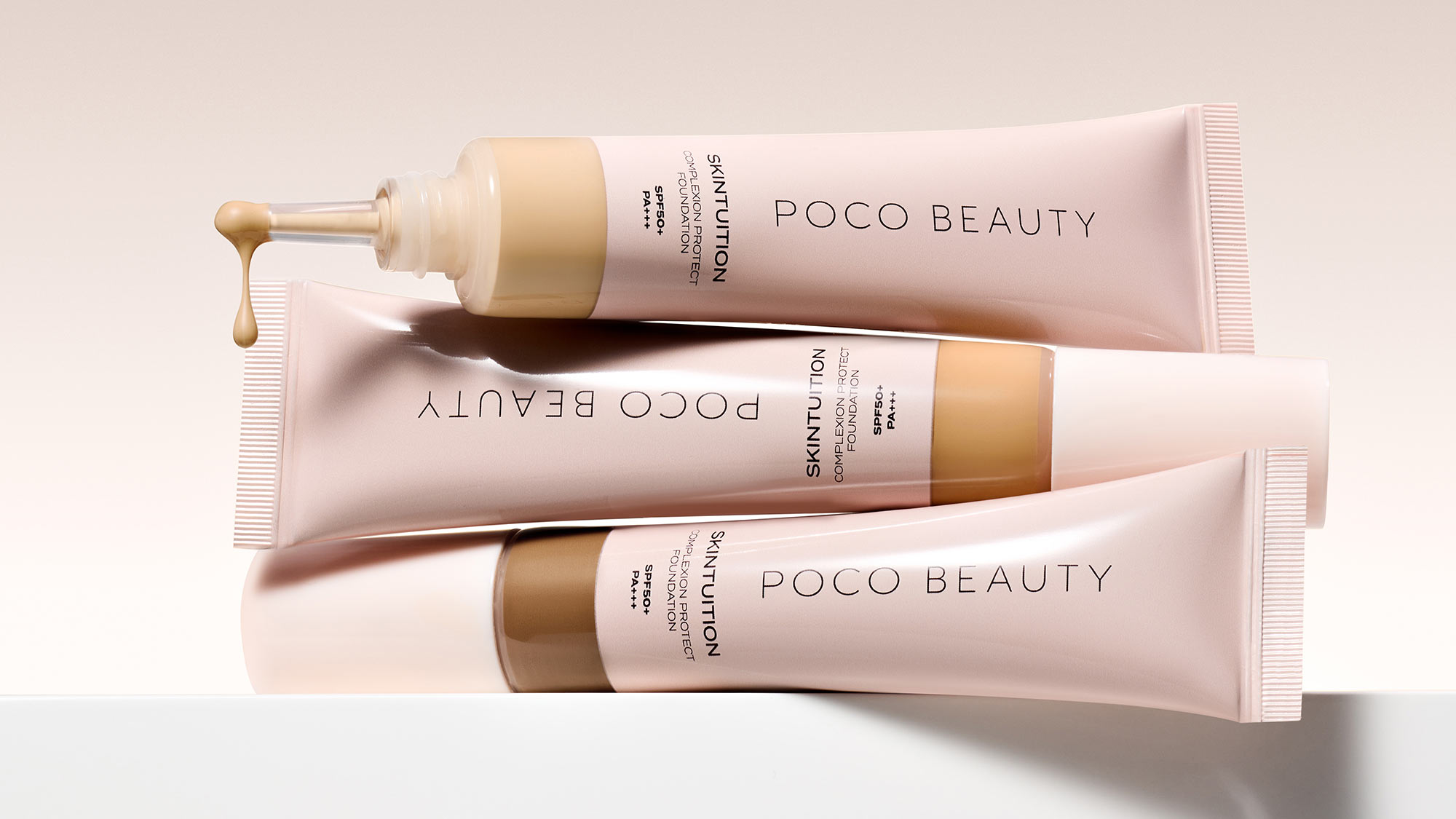 Three Poco Beauty skincare tubes with gold accents displayed on neutral background, including serum, foundation, and treatment products