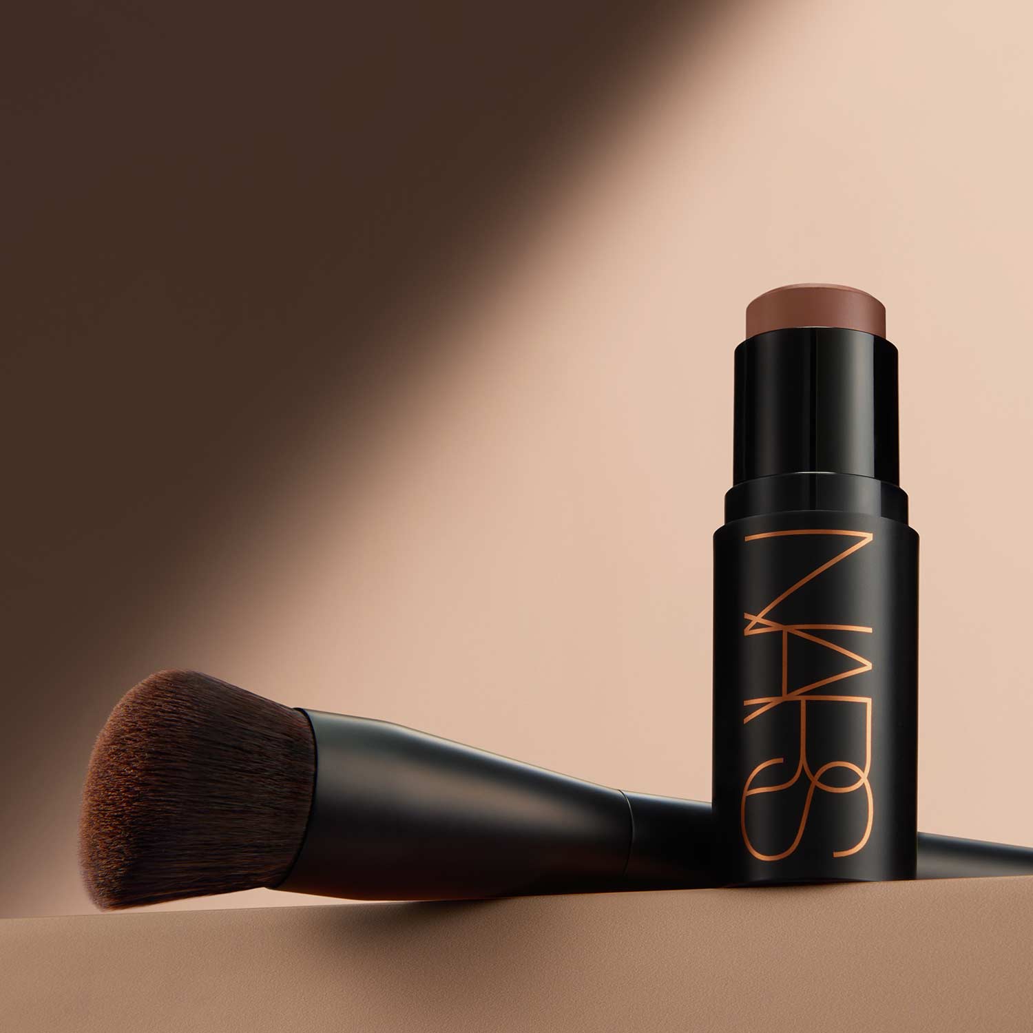 NARS bronzer stick with makeup brush on neutral background