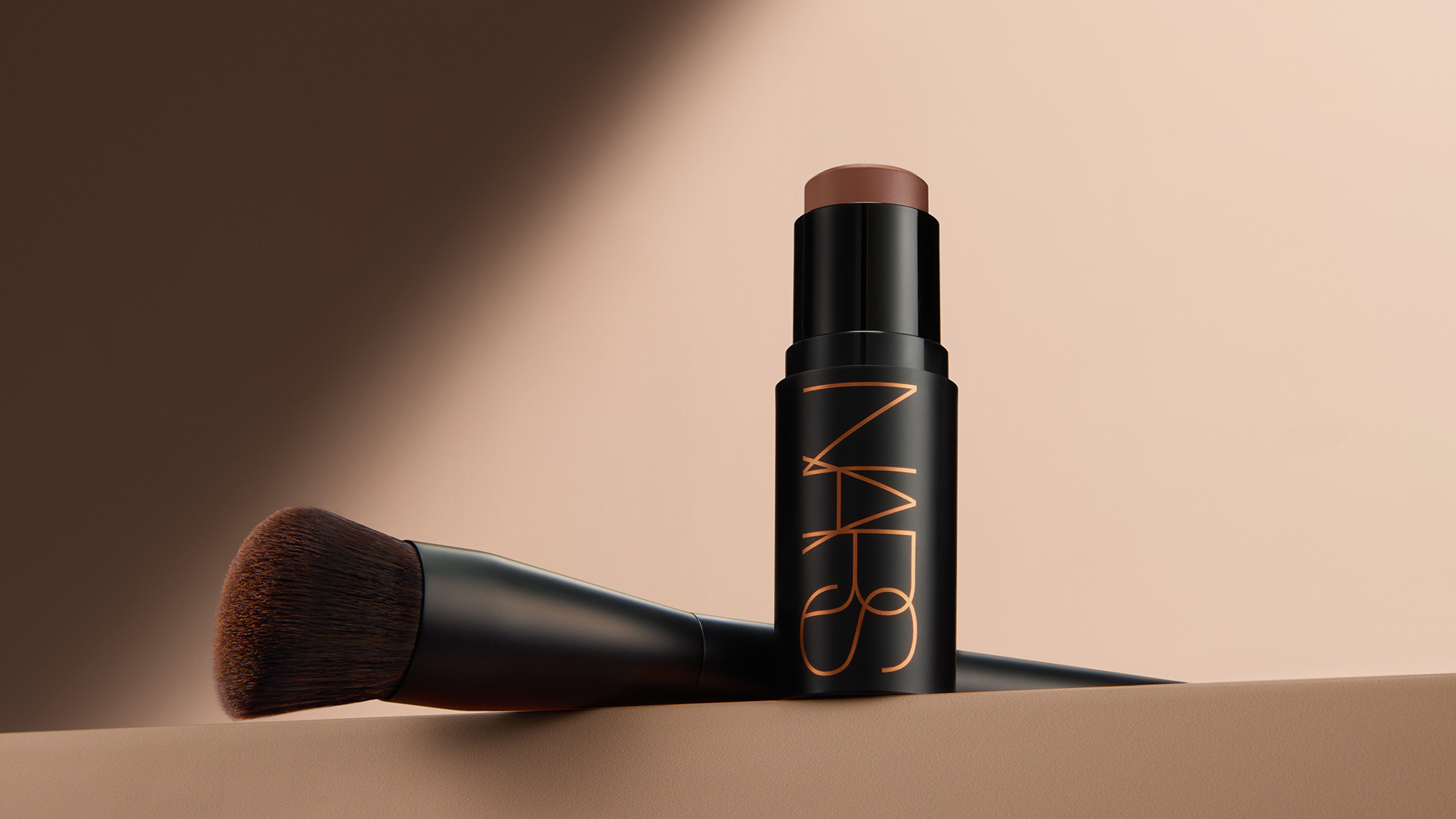 NARS bronzer stick with makeup brush on neutral background