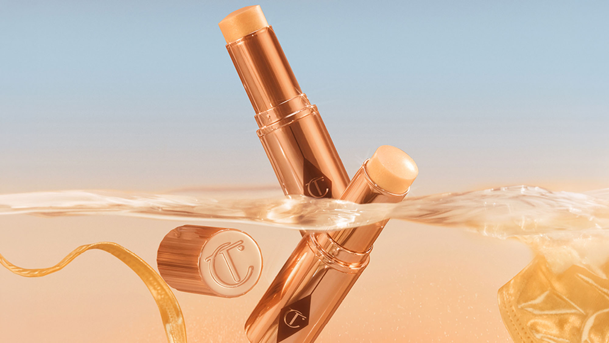 Rose gold metallic lip and cheek product from Charlotte Tilbury displayed with luxury ribbon and water splash effect