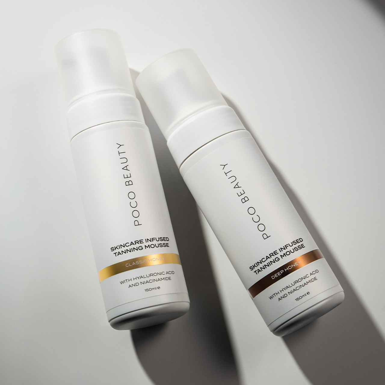 Two white pump bottles of Poco Beauty skincare infused tanning mousse with gold and bronze accent bands