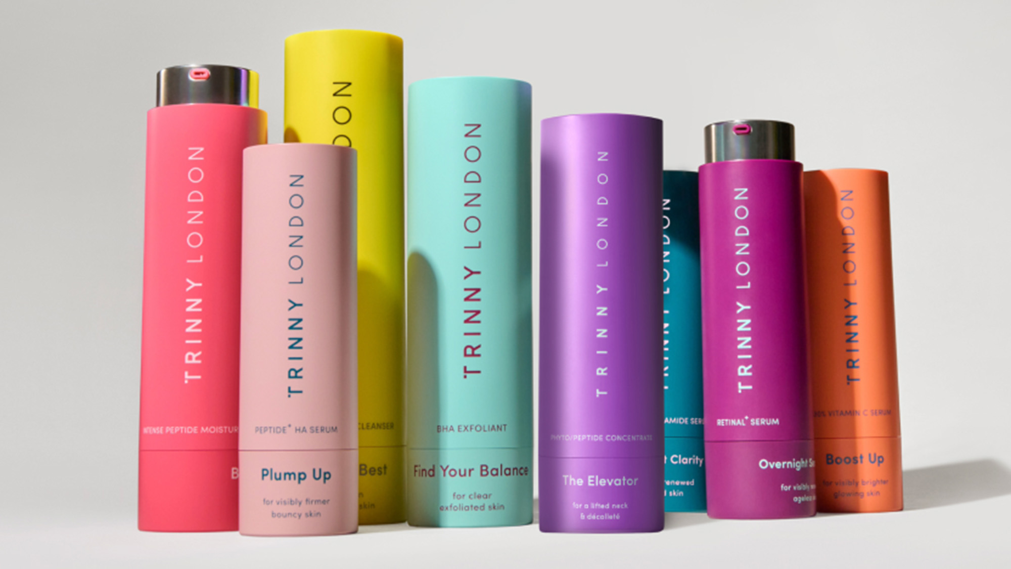 Colourful range of Trinny London skincare serums and treatments in pink, yellow, turquoise, purple, magenta and orange cylinders