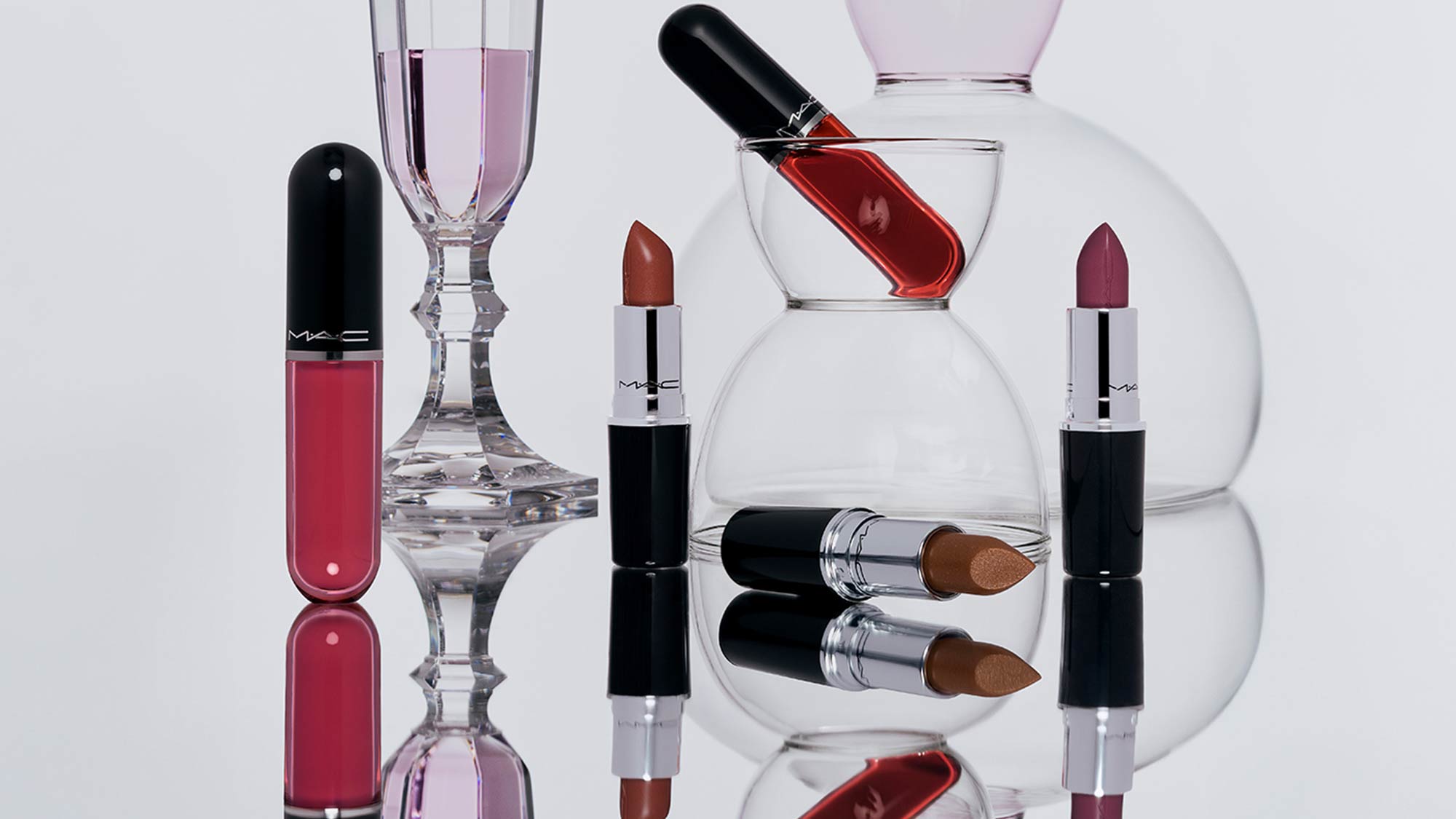 M.A.C Lustreglass Sheer-Shine lipsticks and lip gloss in burgundy and bronze tones, arranged with crystal perfume bottles and nail polish