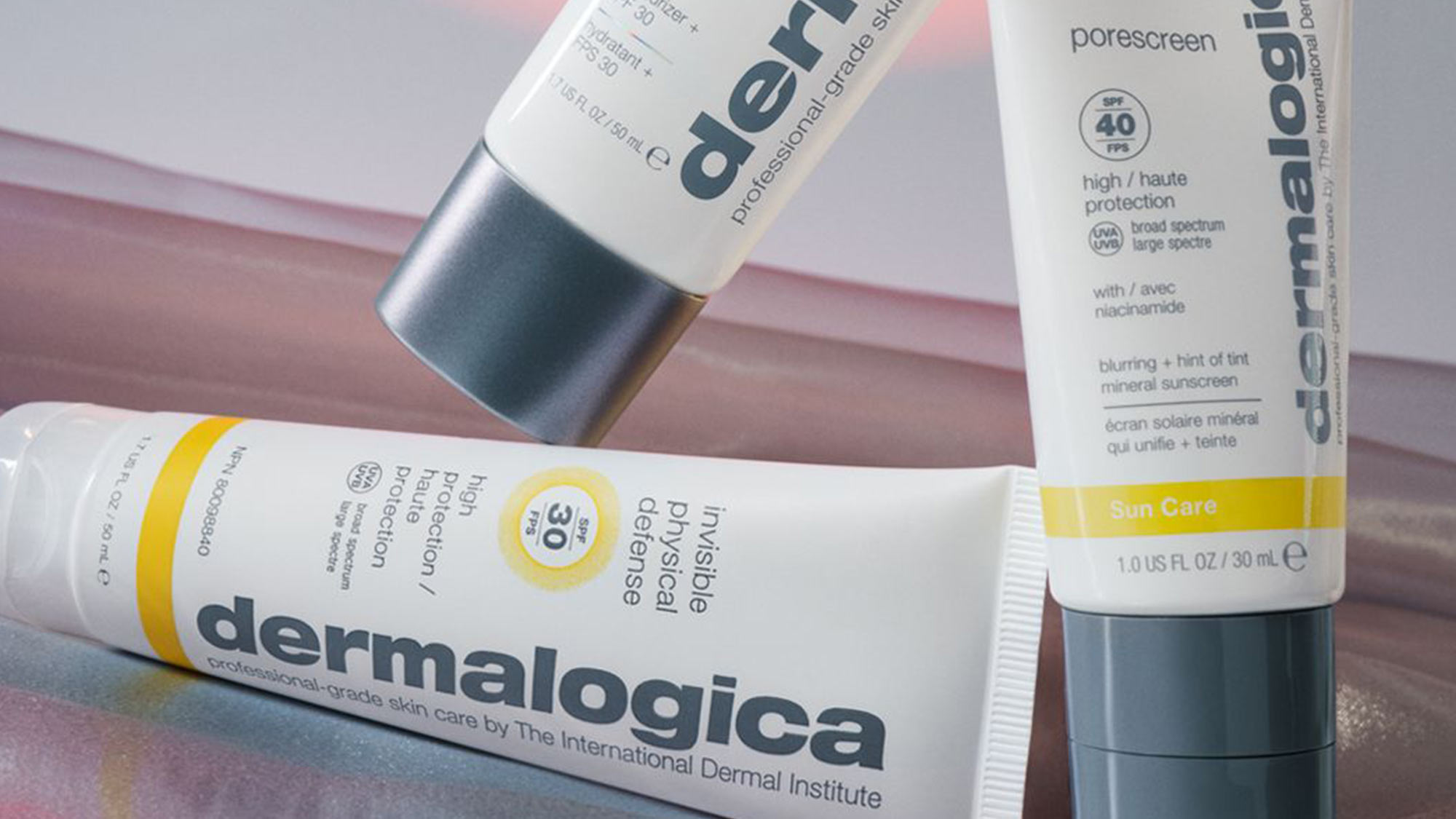 Three Dermalogica skincare bottles displayed on pink and beige background, featuring sun protection and professional-grade skin care products