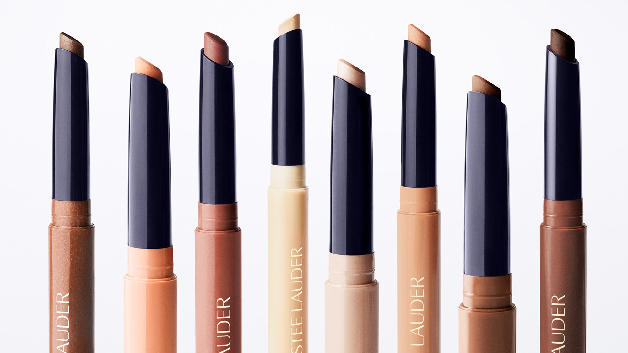 Eight Estée Lauder The Essential Eyeshadow Stick shades in ranging colours from bronze to deep brown against white background