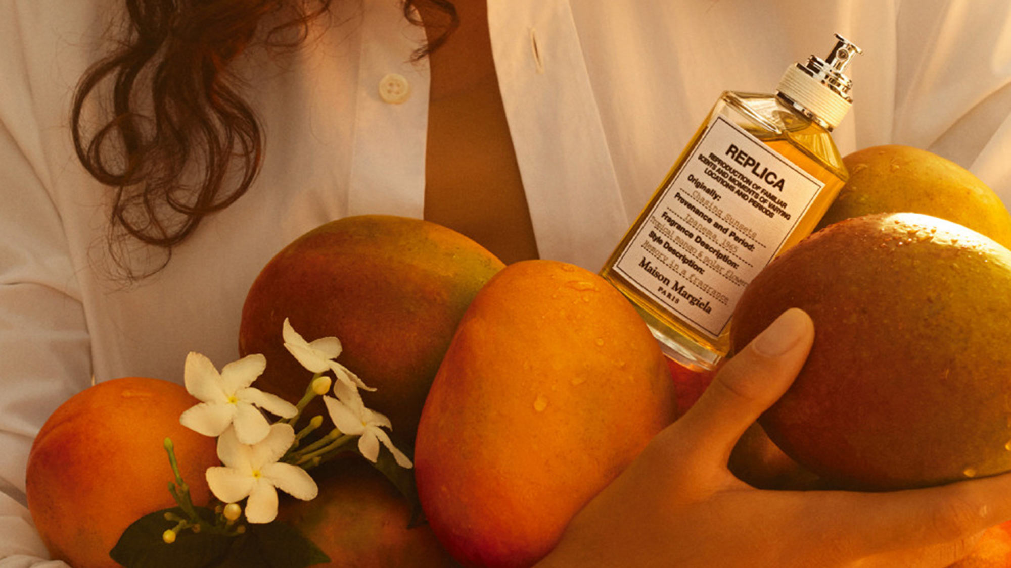 Replica fragrance bottle surrounded by mangoes and white flowers with warm lighting