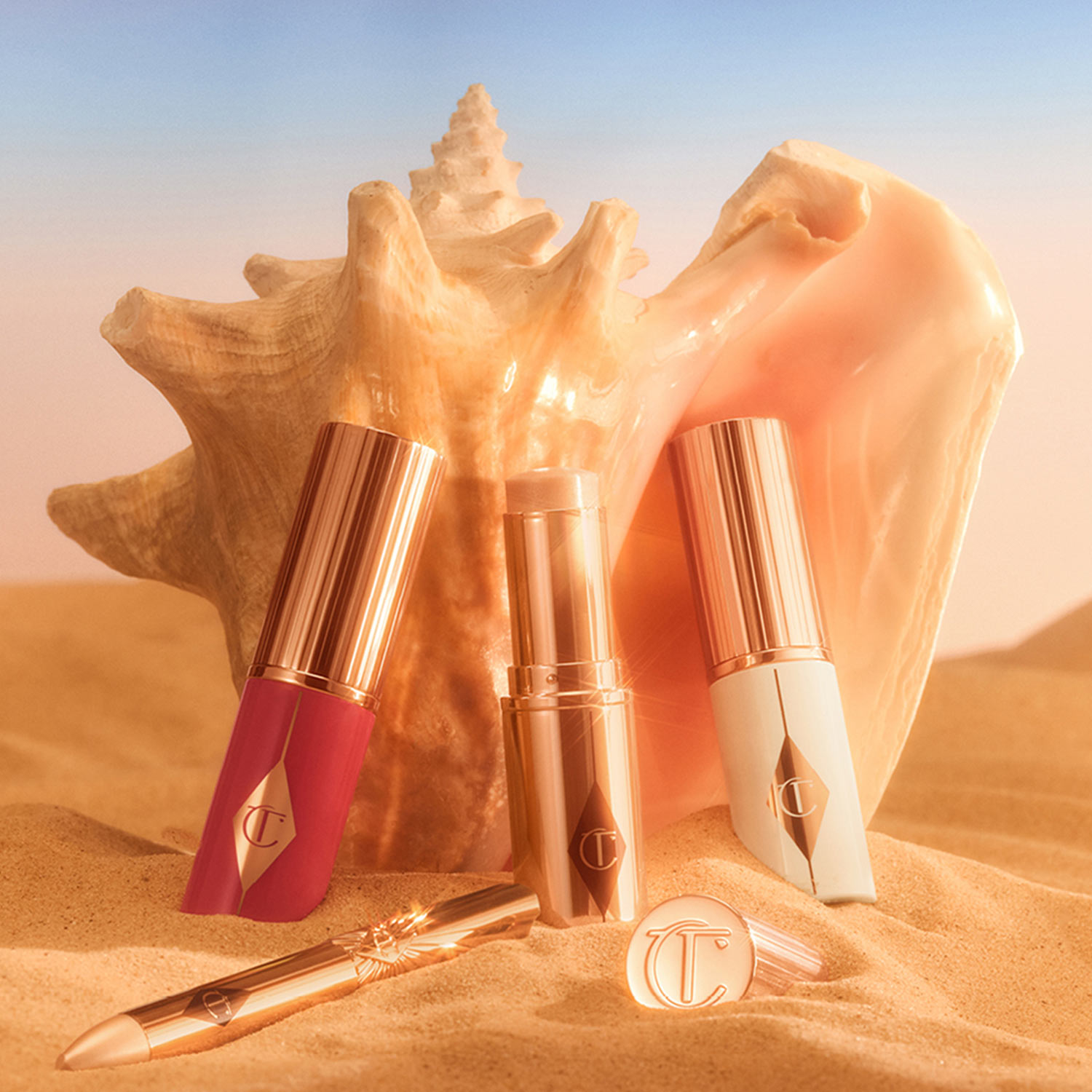 Charlotte Tilbury Unreal Skin foundation and blush products in warm shades displayed on sand with golden hour lighting