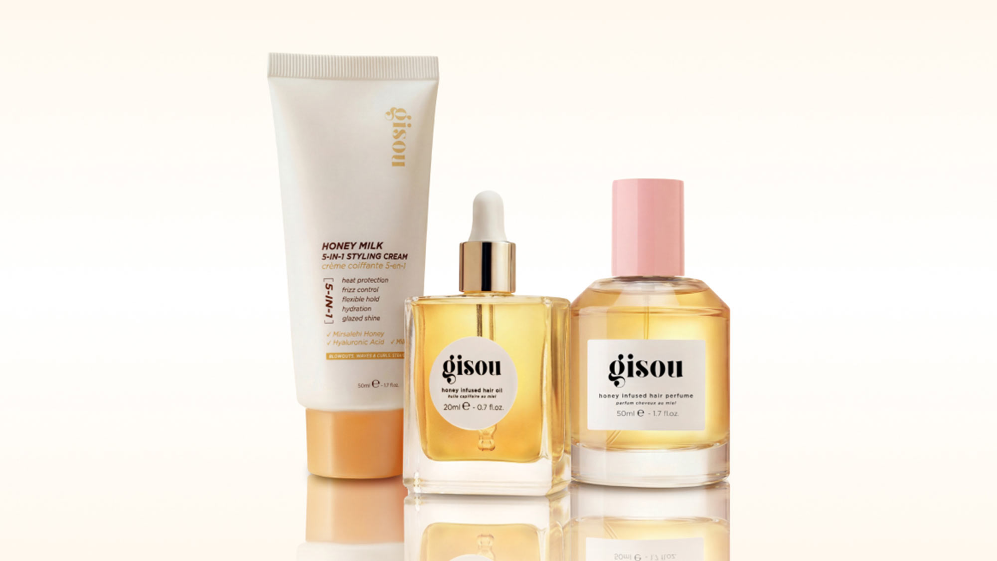 Three honey-infused hair care products by Gisou: styling cream, hair oil, and hair perfume in golden and cream packaging