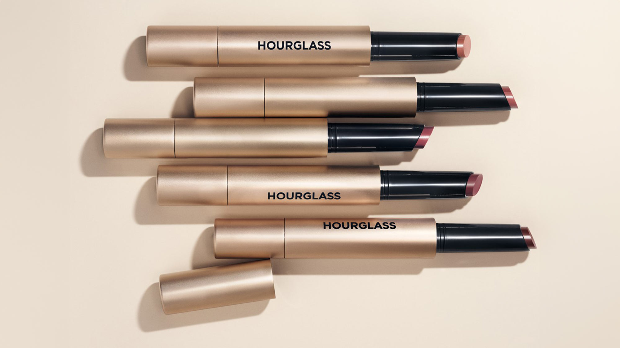 Six Hourglass Blur Balm and Shape & Sculpt Lip Liner products in multiple shades arranged diagonally on neutral background