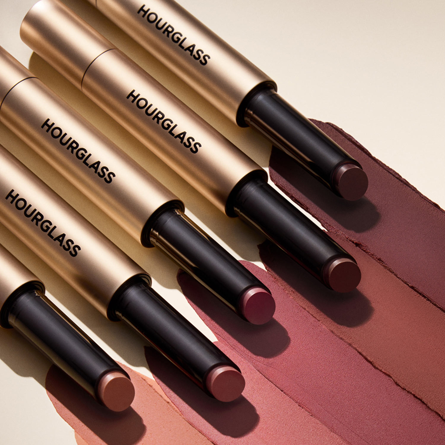 Five Hourglass Blur Balm lip products in assorted shades displayed with colour swatches on beige and mauve fabric
